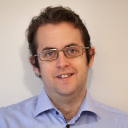 Photo of Luke, a white main with brown hair, wire rimmed glasses, and a blue shirt.